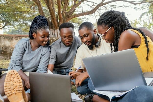 Four young adults sitting outdoors together, looking at laptops.